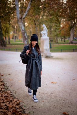 Sonbahar sezonunda parkta yürürken örgü örüp bereyi takan orta yaşlı mutlu bir kadının portresi. Tam uzunluk. 