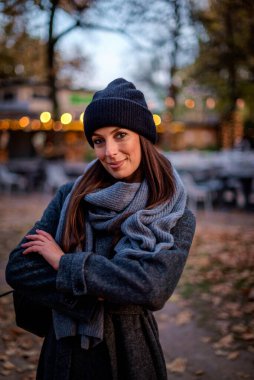 Mutlu orta yaşlı bir kadının portresi. Güz mevsiminde parkta dikilirken sıcak örgü bir eşarp ve bere takıyor.. 