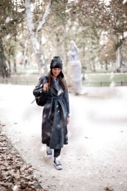 Uzun paltolu ve şapkalı neşeli bir kadın parktaki karın tadını çıkarıyor. Karla kaplı ve soğuk kış havası. Kış tatili Tam boy çekim. 