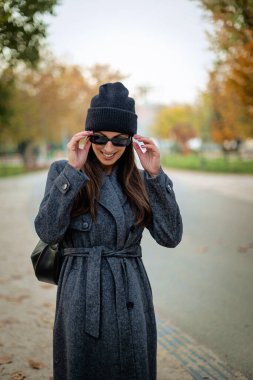 Mutlu orta yaşlı bir kadının portresi. Güz mevsiminde parkta dikilirken sıcak örgü bir eşarp ve bere takıyor.. 