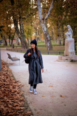 Sonbahar sezonunda parkta yürürken örgü örüp bereyi takan orta yaşlı mutlu bir kadının portresi. Tam uzunluk. 