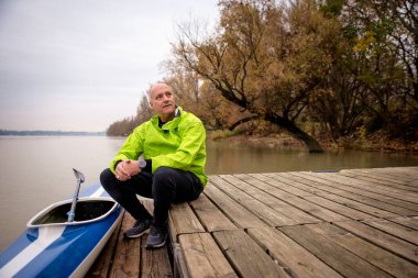 Bir sonbahar günü nehir kenarında oturan aktif bir son sınıf öğrencisi. Kendine güvenen erkek spor giyer ve iskelede dinlenir..