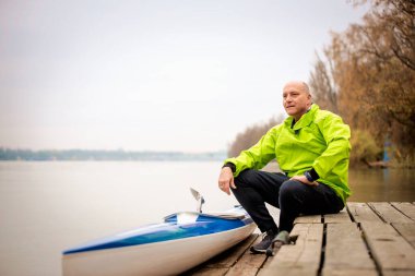 Bir sonbahar günü nehir kenarında oturan aktif bir son sınıf öğrencisi. Kendine güvenen erkek spor giyer ve iskelede dinlenir..