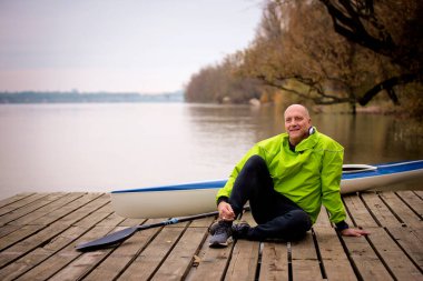 Bir sonbahar günü nehir kenarında oturan aktif bir son sınıf öğrencisi. Kendine güvenen erkek spor giyer ve iskelede dinlenir..