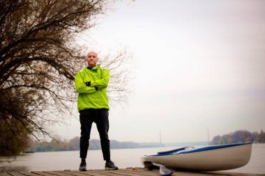 Bir sonbahar gününde nehir kenarında duran aktif bir kıdemli adam. Kendine güvenen erkek spor giyer ve iskelede dinlenir..