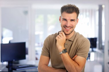 Modern bir ofiste dururken gülümseyen kendinden emin genç bir işadamının portresi. Genç girişimci iş kıyafeti giyer. Yakın çekim..