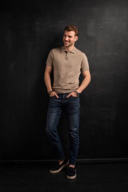 Tecrit edilmiş arka planda duran yakışıklı bir delikanlının yakın çekimi. Uzayı kopyala Polo gömlek ve kot pantolon giyen kendinden emin bir erkek. Tam boy çekim. 