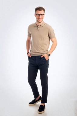 Tecrit edilmiş arka planda duran kendinden emin bir gencin portresi. Yakışıklı erkek iş kıyafeti giyiyor ve kameraya bakıyor. Uzayı kopyala Tam boy çekim.