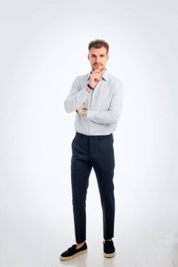 İş kıyafeti giymiş sakallı bir gencin portresi ve izole edilmiş beyaz arka plana karşı ayakta duruyor. Stüdyo çekimi, kopyalama alanı. Tam boy. Eller çenede.. 