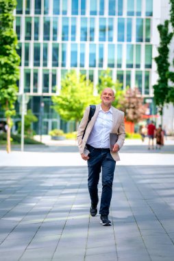 Şehirde iş bölgesinde yürüyen yakışıklı bir adam. Orta yaşlı iş adamı iş kıyafeti giyiyor ve elinde bilgisayar laptopu tutuyor..