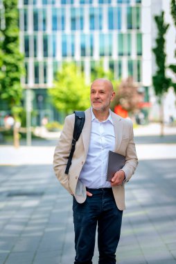 Şehirde iş bölgesinde yürüyen yakışıklı bir adam. Orta yaşlı iş adamı iş kıyafeti giyiyor ve elinde bilgisayar laptopu tutuyor..