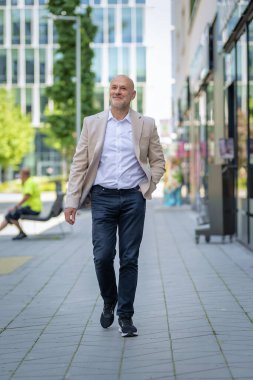 Kendine güvenen orta yaşlı bir adamın modern bir iş diskinde sokaklarda yürümesi. İş kıyafeti giyen beyaz bir adam..