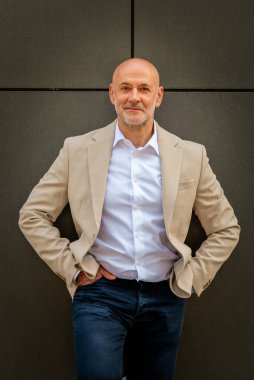 Gri bir duvarın önünde caddede duran orta yaşlı bir adam. İş kıyafeti giymiş yakışıklı bir iş adamı..