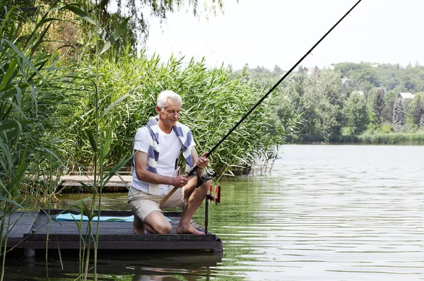 Senior man sitting at pier and fishing. — Stock Photo, Image