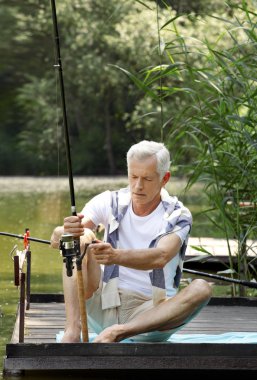 Senior man sitting at pier and fishing.