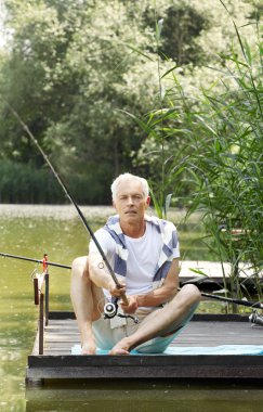 Senior man sitting at pier and fishing.