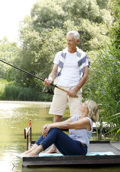 Happy senior couple fishing at lakeshore — Stock Photo, Image