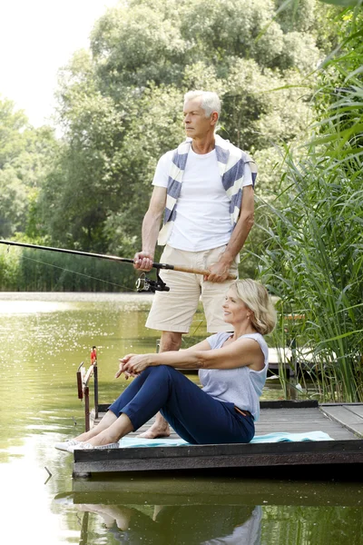 Happy senior couple fishing at lakeshore — Stock Photo, Image