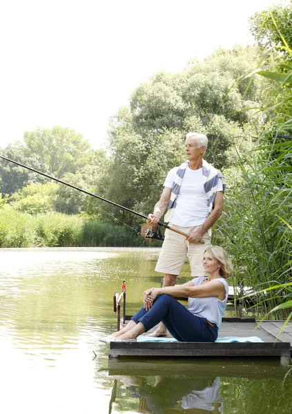 Happy senior couple fishing at lakeshore — Stock Photo, Image