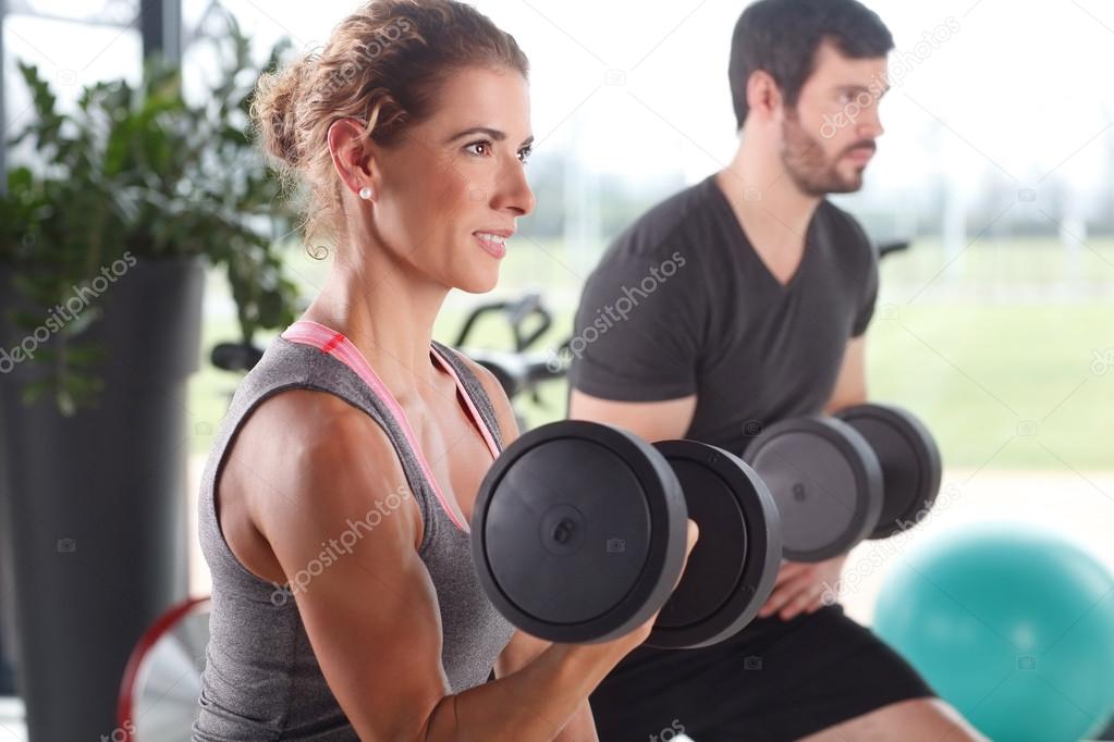 Woman and man lifting barbells at fitness center