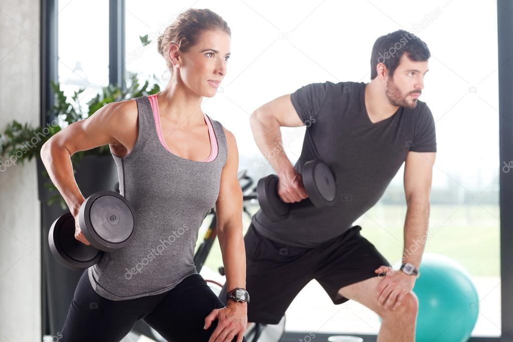 Woman and man lifting barbells at fitness center