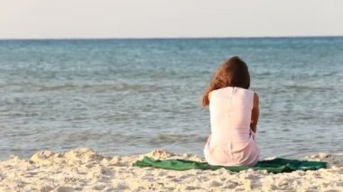 Kız sahilde oturuyor.