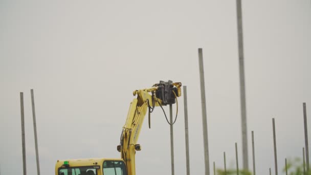 Een graafmachine met een speciaal apparaat aandrijft betonnen pijlers — Stockvideo