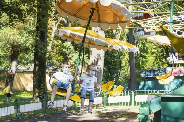 Enfants en masques médicaux monter un carrousel — Photo