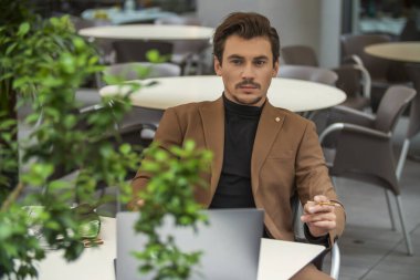 Takım elbiseli bir adam masada sigara içiyor.