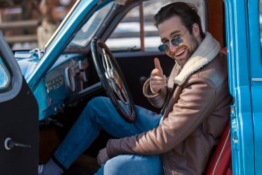 Eski bir arabada oturan bir adam.