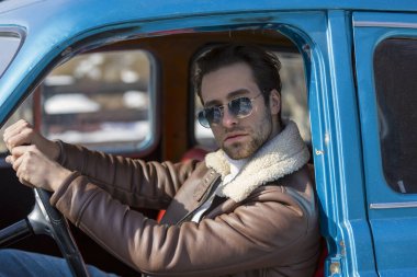 Eski bir arabada oturan bir adam.