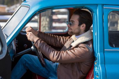 Eski bir arabada oturan bir adam.