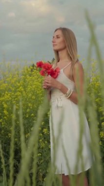 Gün batımında haşhaş tarlasında yürüyen güzel genç bir kadın. Dikey yönelim