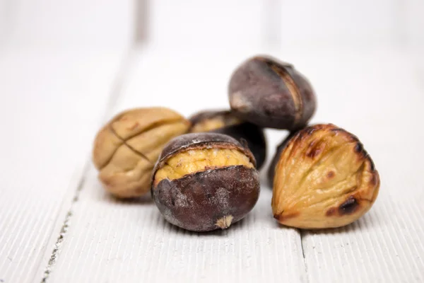 Castagne tostate calde su sfondo di legno bianco — Foto Stock