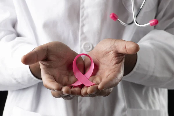 dark skin doctor with pink stethoscope and pink awareness breast cancer ribbon, on a black background.