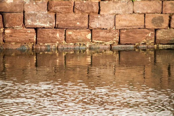 Red stone brick wall from a building creating a reflection on the water — Stock Photo, Image