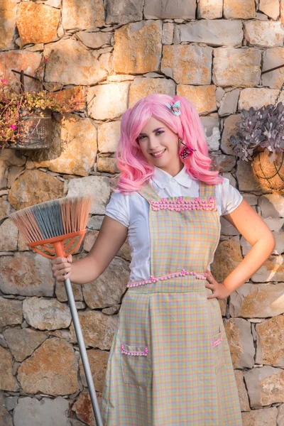 Giovane ragazza con una scopa e una parrucca rosa . — Foto Stock