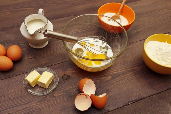 Eggs with milk and other natural ingredients for making dough for baking on a wooden table.