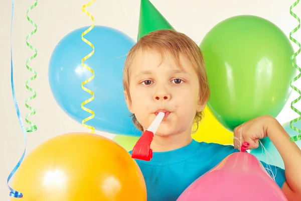 Little cute boy in holiday hat with whistle and festive balloons and streamer