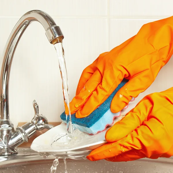 Hands in gloves with sponge wash the dishes under running water in kitchen