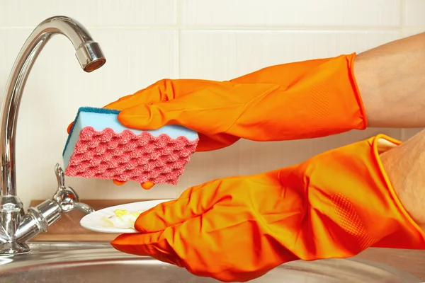 Hands in gloves with sponge and dirty plate over sink in the kitchen