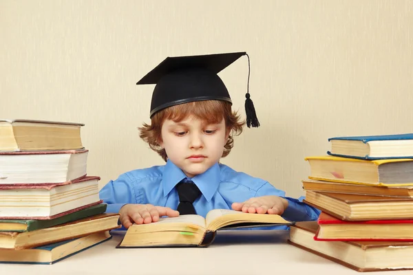 Little serious boy in academic hat reading old books