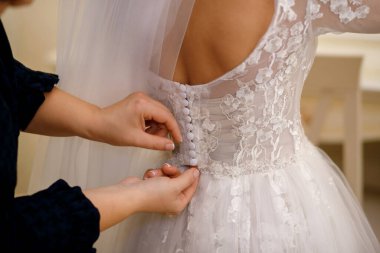 Düğün gününde, nedime gelinin gelinliğini giymesine yardım eder. Vurgu, tasarımcı beyaz elbisesinin düğmelerini bağlayan ellerde. Gelini damada hazırlıyorum.