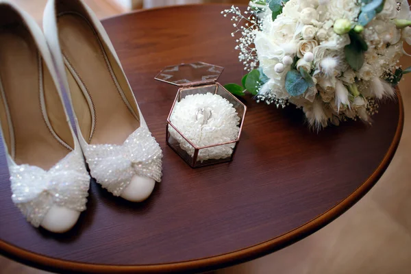 Wedding accessories in the form of a bouquet, rings and shoes on a wooden table. Gathering the bride in the morning and preparing for the wedding day. Gold wedding rings top view