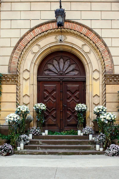 Wedding ceremony with natural white flowers against the background of a huge antique wooden door. Wedding day in an old European city, the bride and groom prepare to enter the official ceremony