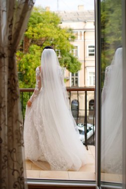 Beyaz gelinlik ve duvak giymiş gelin balkona çıktı ve piriloyu tutuyor. Bir kadın, damadın düğün günü gelmesini bekliyor. Metin için boş alan