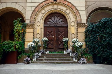 Doğal beyaz çiçeklerle düğün töreni ve arka planda kocaman ahşap bir kapının mumları. Eski bir Avrupa şehrinde düğün gününde. Metin için boş alan