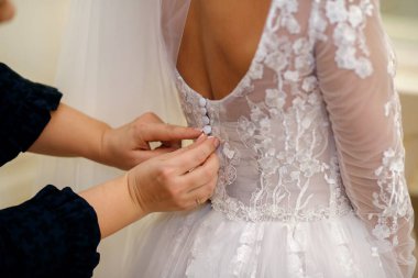 Düğün gününde, nedime gelinin gelinliğini giymesine yardım eder. Vurgu, tasarımcı beyaz elbisesinin düğmelerini bağlayan ellerde. Gelini damada hazırlıyorum.