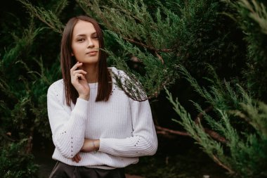 Ardıç süren esmer bir kadının portresi. Parkta bir fotoğrafçıya poz veren ve gülümseyen güzel bir kız. Kız beyaz bir kazak giyiyor. Metin için boş alan