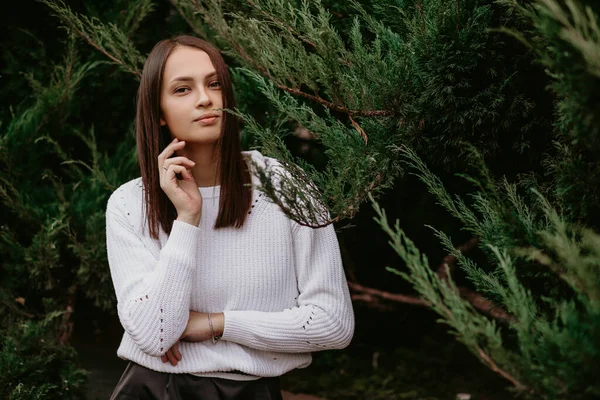 Ardıç süren esmer bir kadının portresi. Parkta bir fotoğrafçıya poz veren ve gülümseyen güzel bir kız. Kız beyaz bir kazak giyiyor. Metin için boş alan